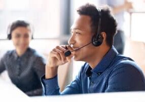 Smiling young african businessman call center agent wear wireless headset laugh at workplace, cheerful happy black male telemarketer operator have fun at work break in customer service support office
