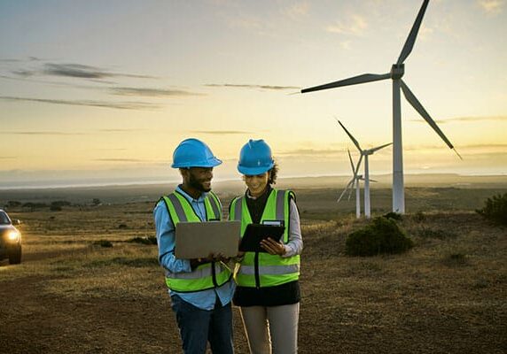 Wind turbine, engineering team and laptop on night farm for clean energy, power and electricity. Electrician or technician man and woman in nature for windmill and eco environment online maintenance