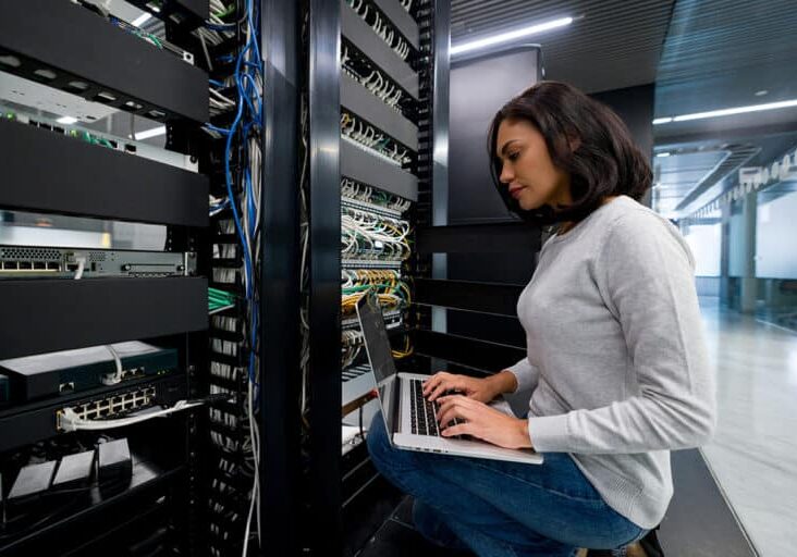 Female IT support technician fixing a network server at an office - technology concepts