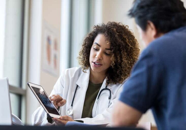 The mid adult female doctor uses the digital tablet to show the x-ray to the unrecognizable senior man.