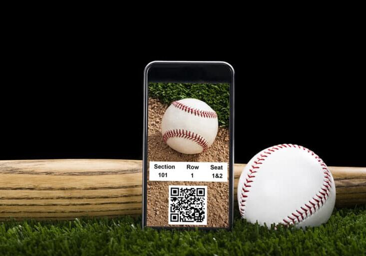 A Smart Phone displaying online baseball tickets with QR/Bar code, sitting on the turf with a new baseball and bat against a black night sky background