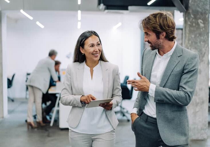 Shot of two coworkers having a discussion in modern office. Businessman and businesswoman in meeting using digital tablet and discussing business strategy. Confident business people working together in the office. Corporate business persons discussing new project and sharing ideas in the workplace.