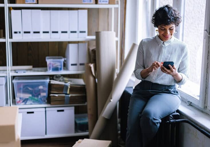 A beautiful smiling female Latin-American entrepreneur using her mobile phone to take orders for her small business.