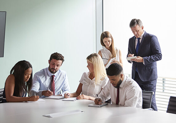Group Collaborating On Task At Graduate Recruitment Assessment Day Whilst Being Observed By Recruitment Team
